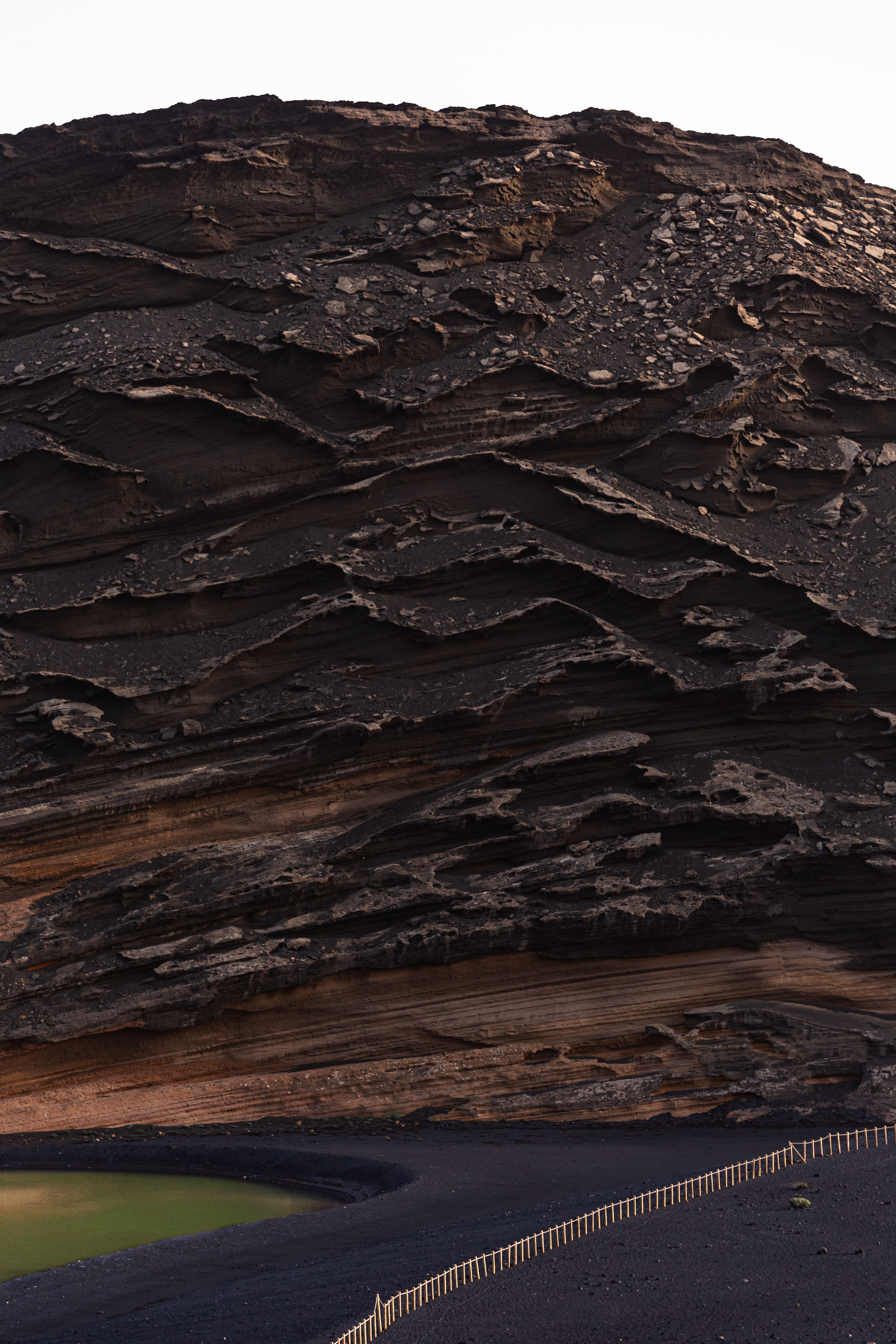 Strange rock formations on a hill above a green lake, with black sand surrounding