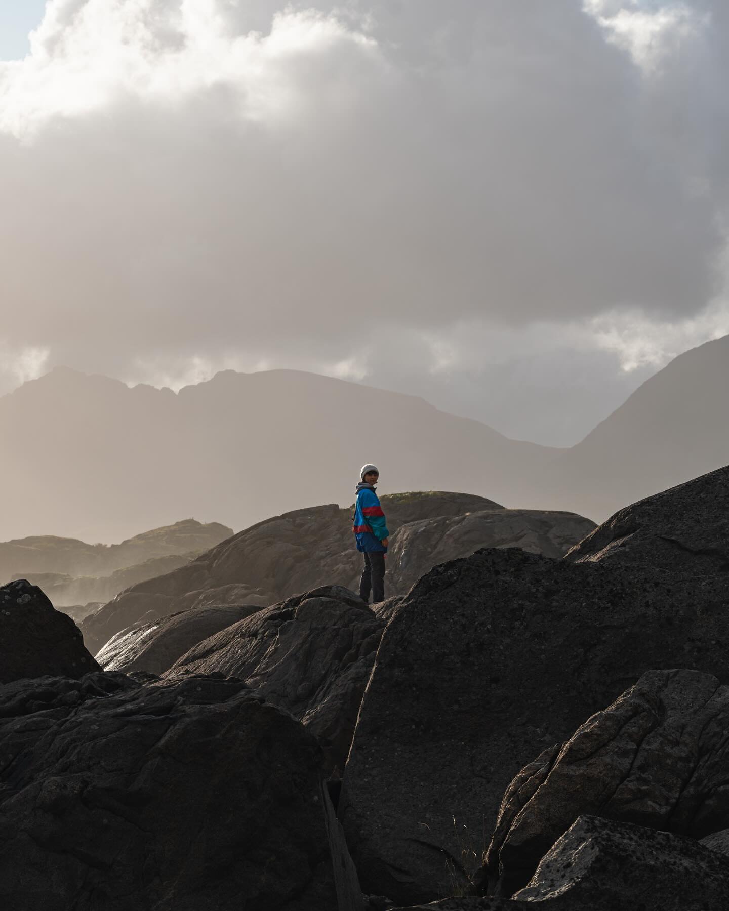 A long, empty road stretches into the distance under a dark, cloudy sky with mountains in the background.
