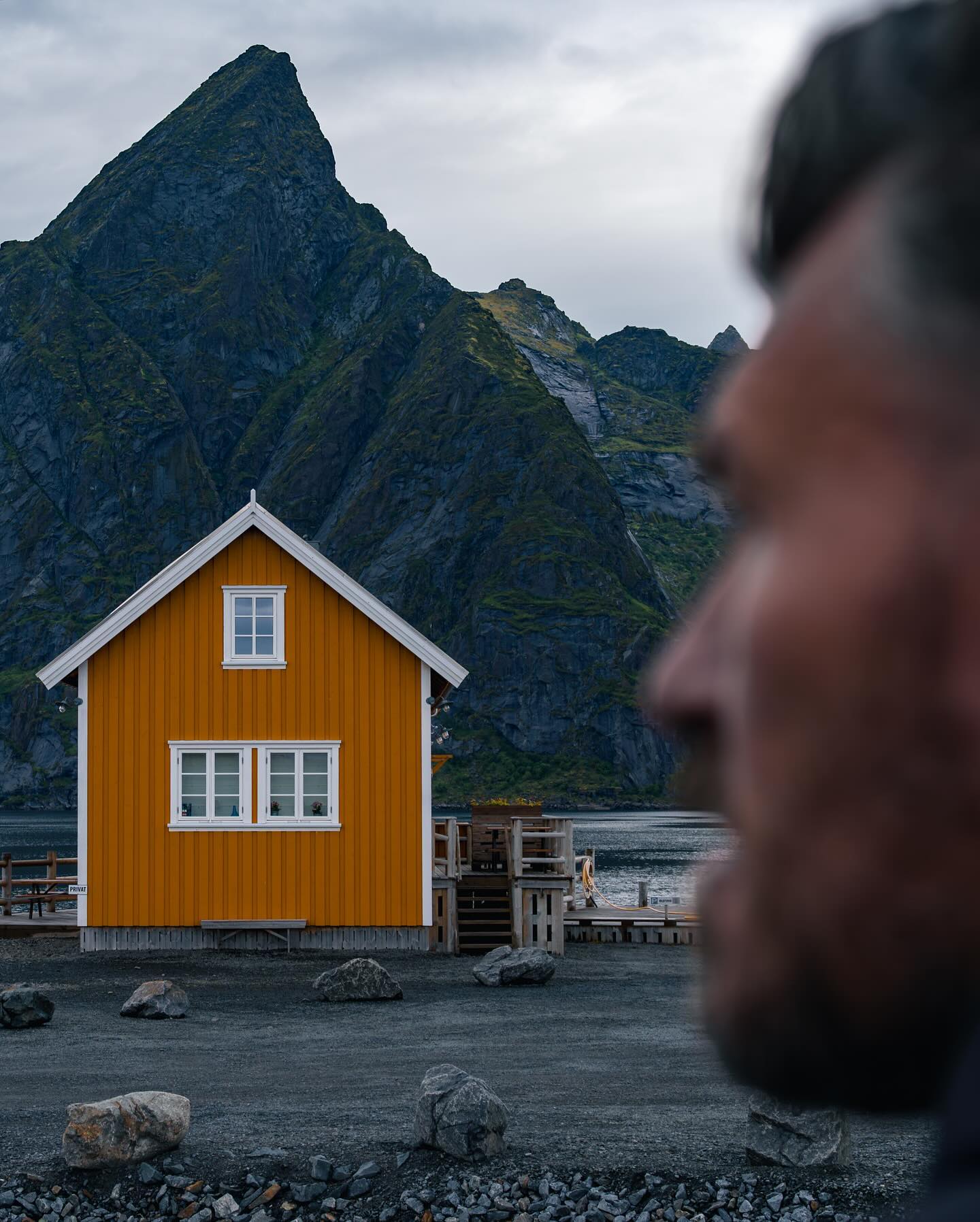 An orange and white fishing hut, with a mountain peak behind.
