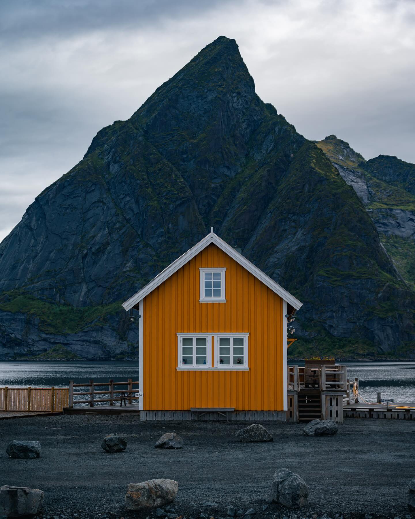 An orange and white fishing hut, with a mountain peak behind.