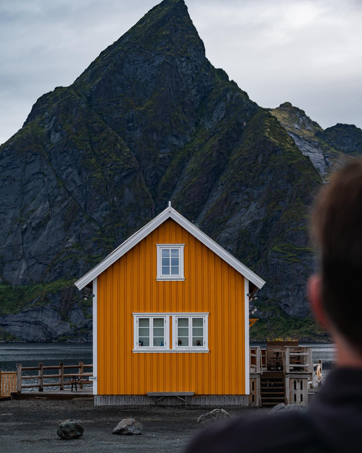 An orange and white fishing hut, with a mountain peak behind.